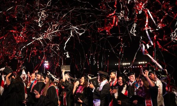 Image shows graduates celebrating under streamers at commencement. 