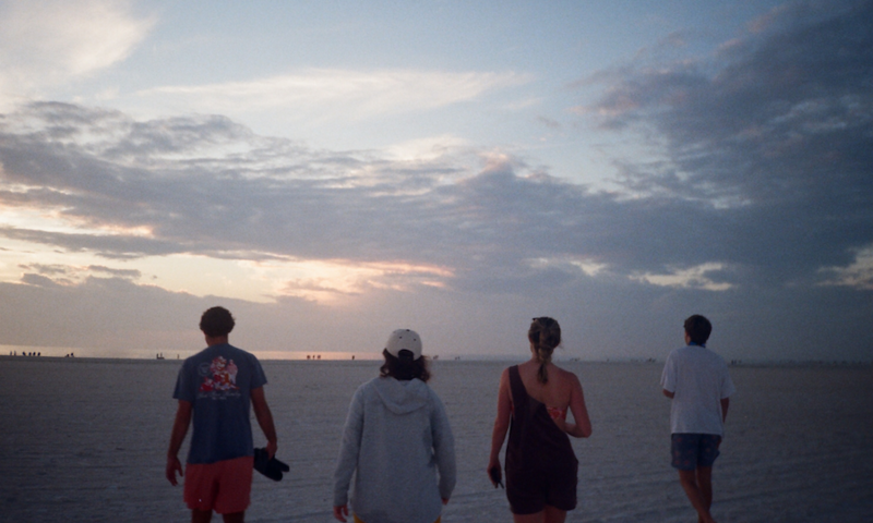 four friends walking on the beach at sunset