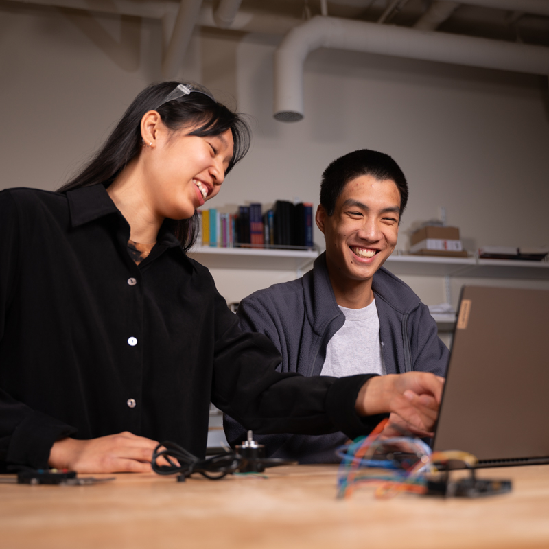 Two engineering students talking and sitting at a table in front of a laptop