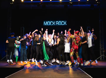 Students in costumes celebrating together on stage during Mock Rock.