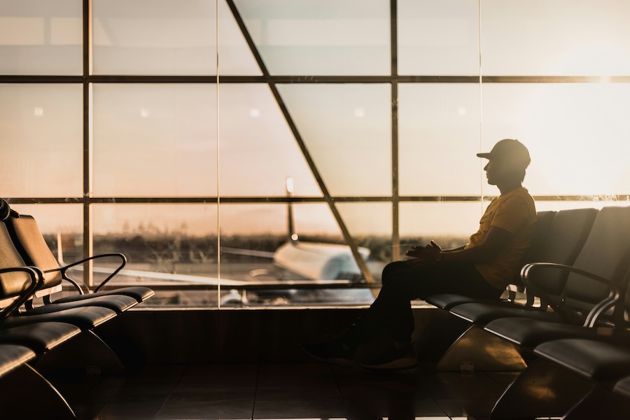 A man sitting at an airport with a plane visible through large windows.