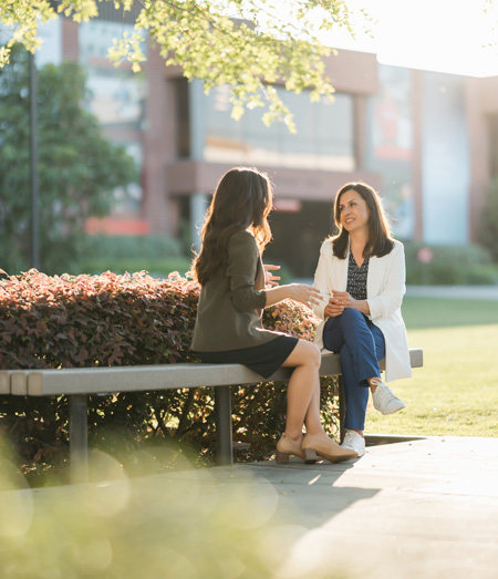 A student and mentor sit on a bench by Metzger Lawn