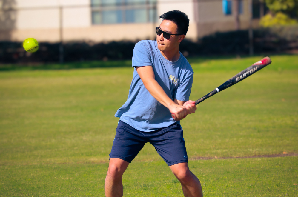 A Biola University student swinging a bat during an intramural baseball game, about to strike the ball
