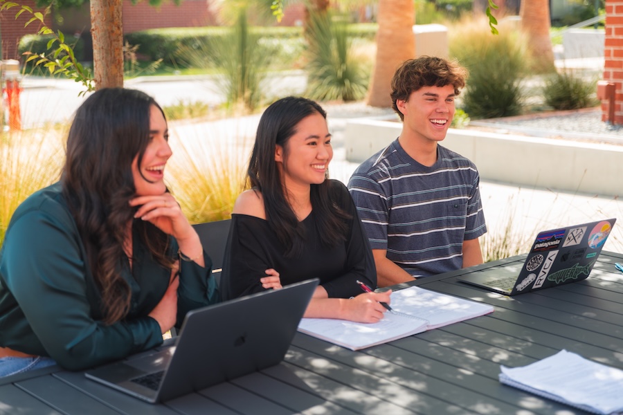 Students sitting together laughing at a table outside.