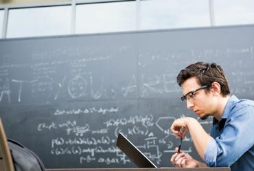 Student working on a computer with calculations on blackboard