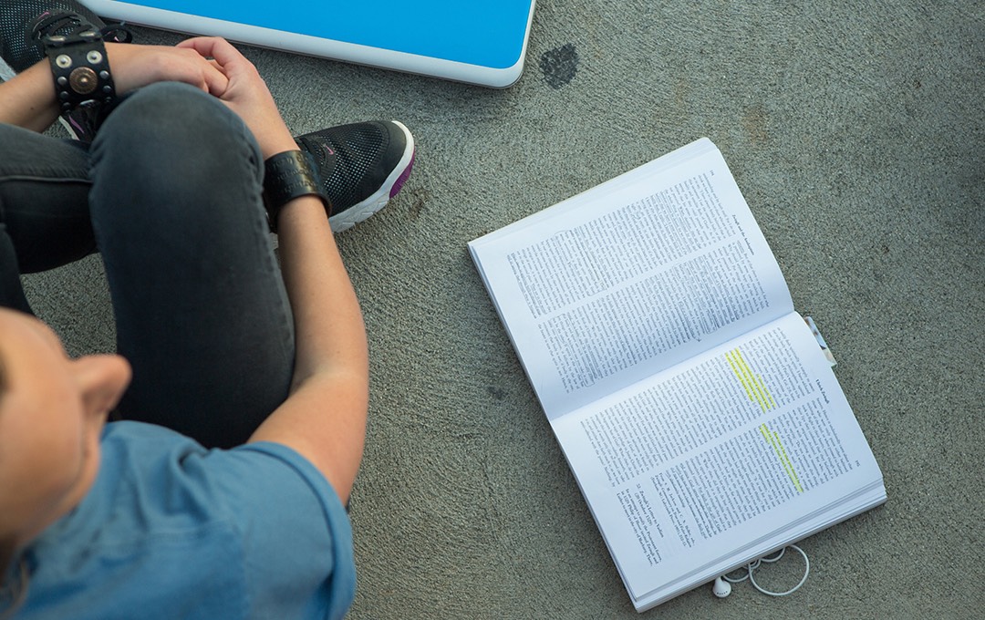 A text book with a few highlighted lines lays open next to a student.