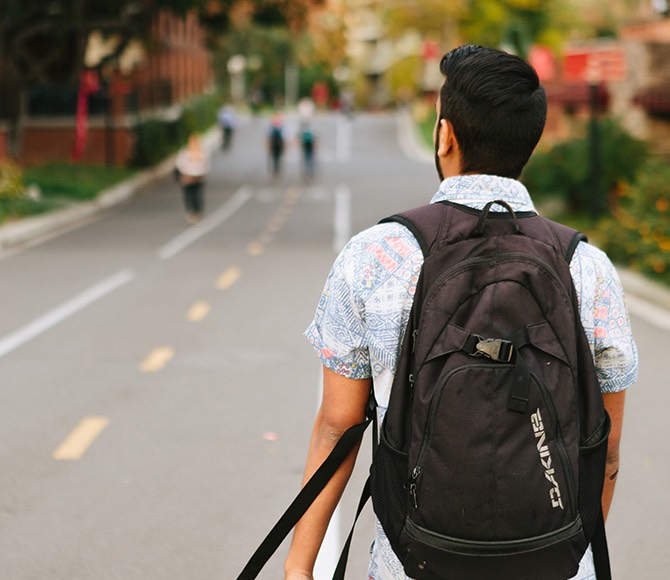 A student wearing a backpack walks down the path by the cafeteria.
