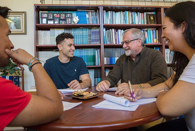 A group of students meets with a professor in his office.