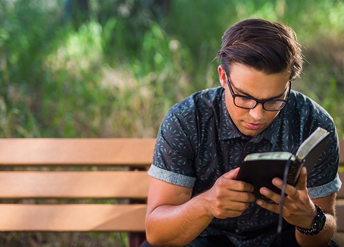 A student reads the Bible on a park bench.