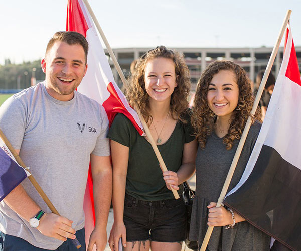 Three students smile while each of them holds a flag from different countries.