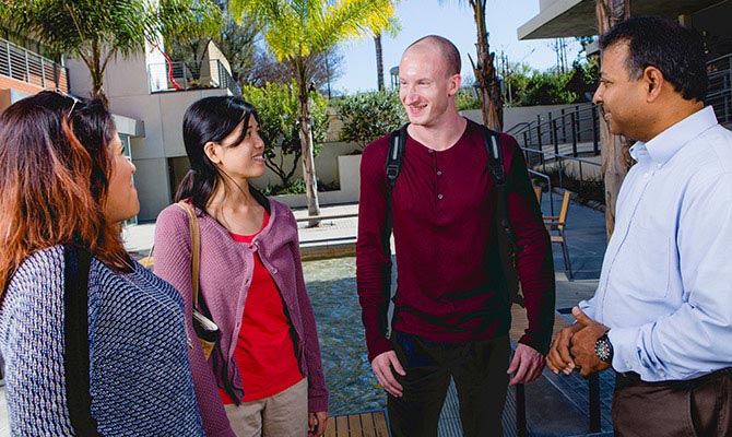 A group of students talk with a professor in the Talbot East Plaza