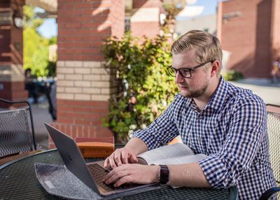 Male student working on laptop outside