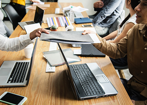 Two people passing a paper folder above laptop screens