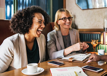 two women in business attire talking and laughing