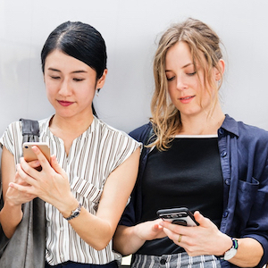 Two women staring at their cell phones.