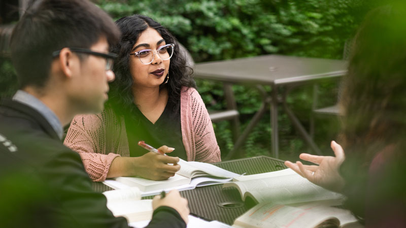 Three people studying and discussing with open books and pens