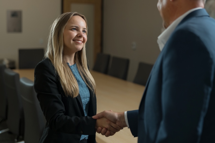 University alumnus and business professional exchange a handshake in a professional setting, symbolizing networking, mentorship, and employment opportunities.