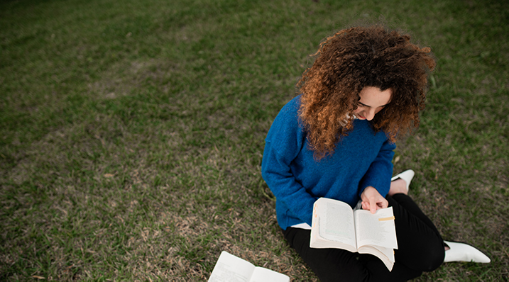 student reading a book on the lawn