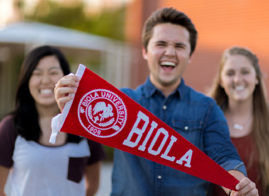 students laughing with a Biola pennant flag