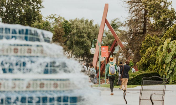 Students walking near the bell tower with a fountain in the foreground