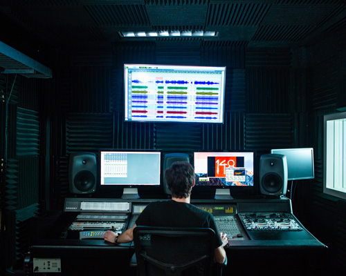 Student sits at a desk mixing audio in a studio. 