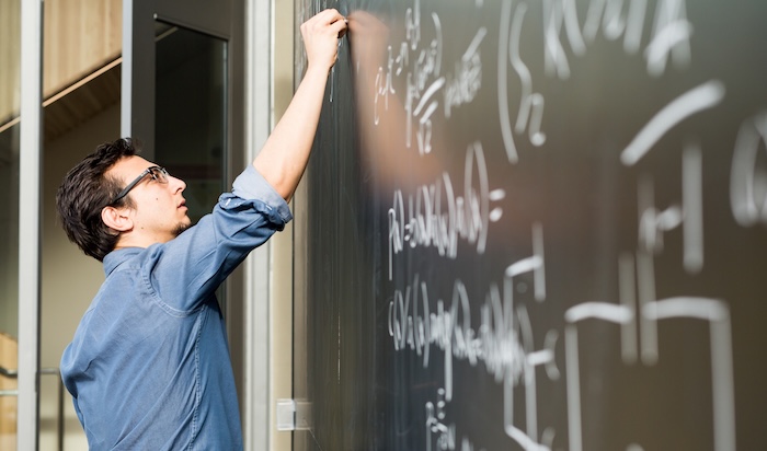 A student is writing down an equation on a chalk board.
