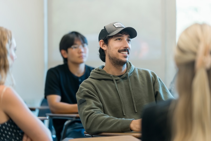 Students listen attentively to a lecture delivered by a female professor in a classroom setting.