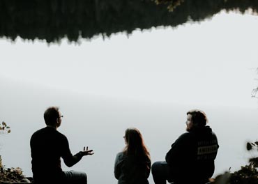 Three people sitting and talking by a lake