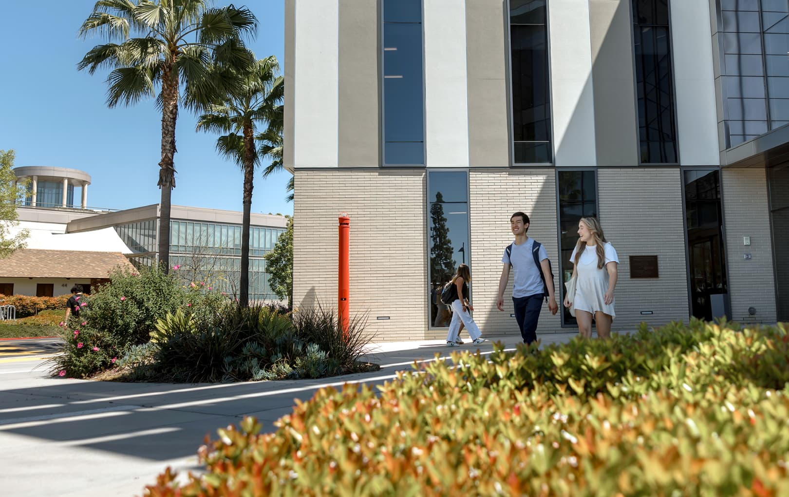 Students exiting a large modern building with palm trees in the background