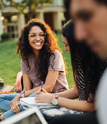A student smiles while studying with a group on a lawn