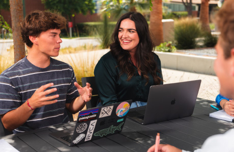 students with laptops talking at a table
