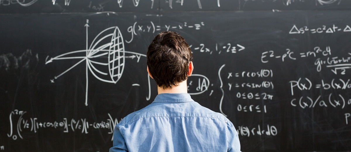 Engineering student standing in front of a chalkboard and looking at the equations written on it