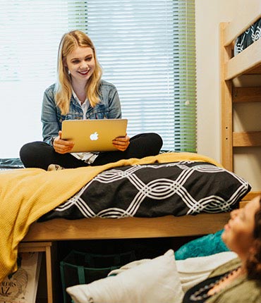 Roommates laugh while they study in their dorm room.