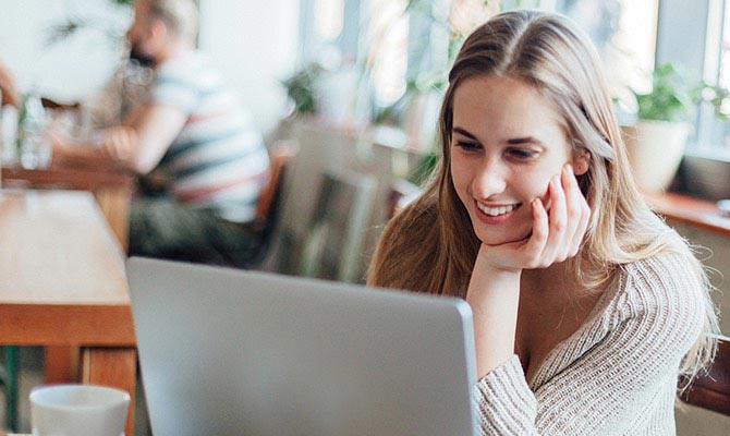 A student smiles while working on a laptop at a coffee shop