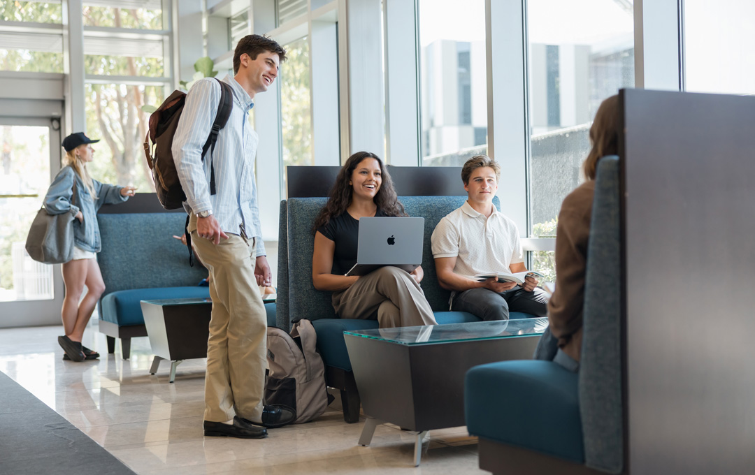 Students sitting and talking with laptops and books