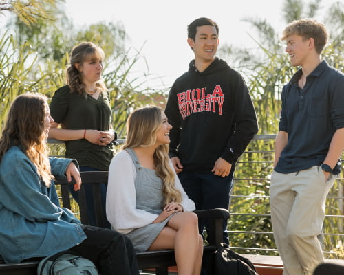 Group of students wear Biola apparel talking together outside on the Riady Rooftop Garden.