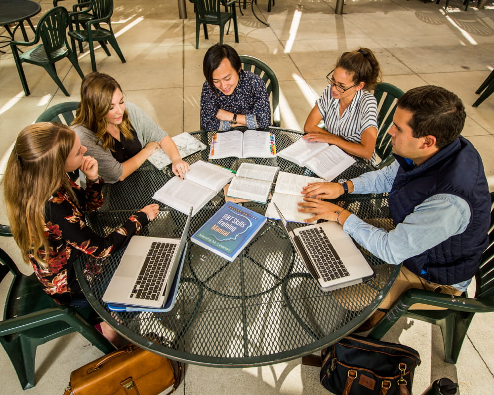 Group sits around a table discussing topic with different books and digital resources.