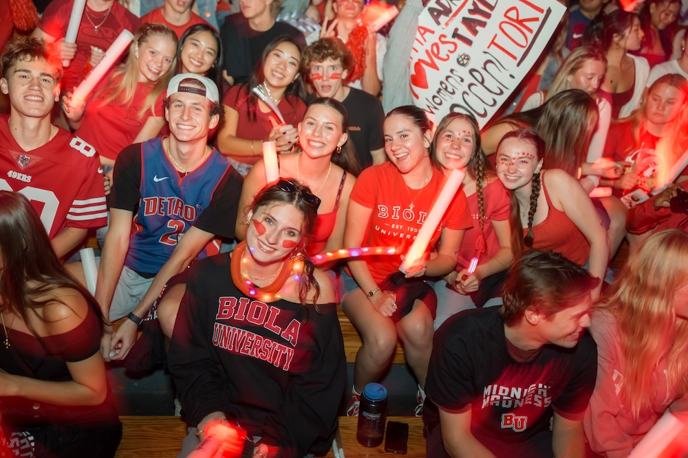 A crowd of Biola University students sitting in a gym, all wearing red for a sporting event.