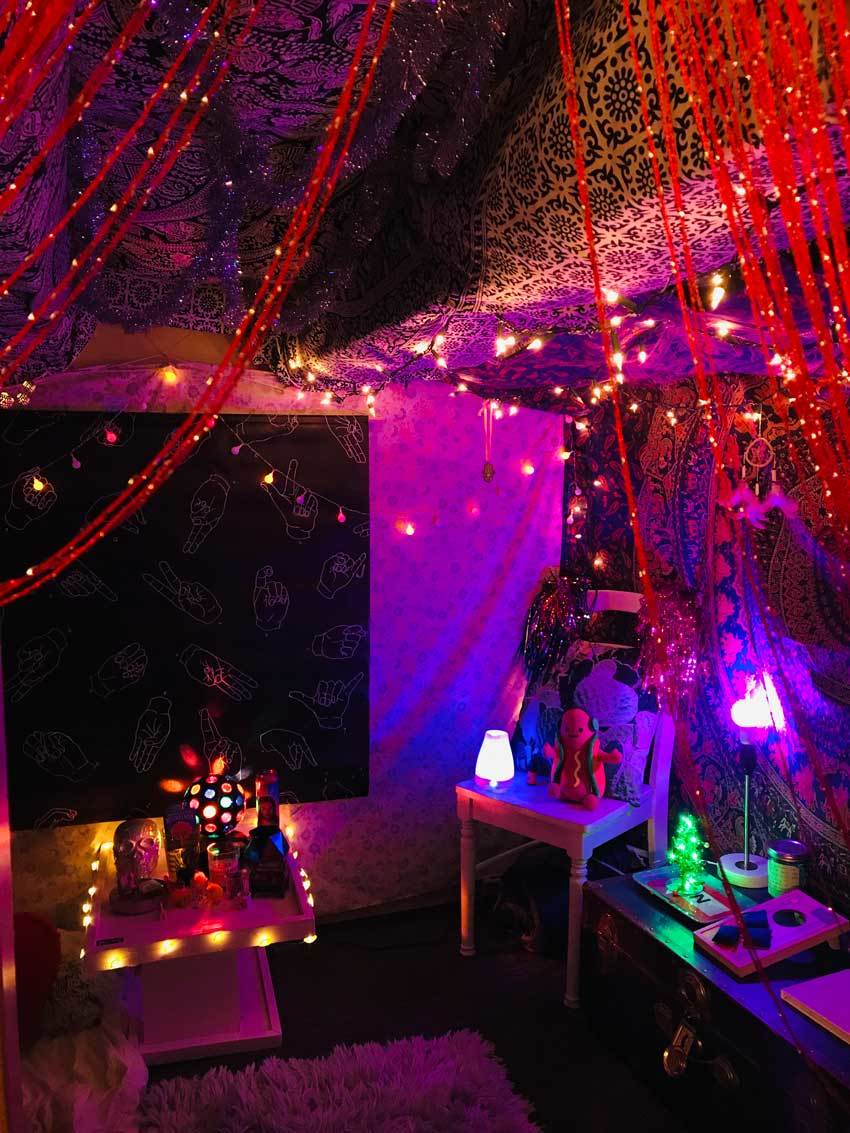 The desk area under a lofted bed features brightly patterned cloth drapings and many small lights.