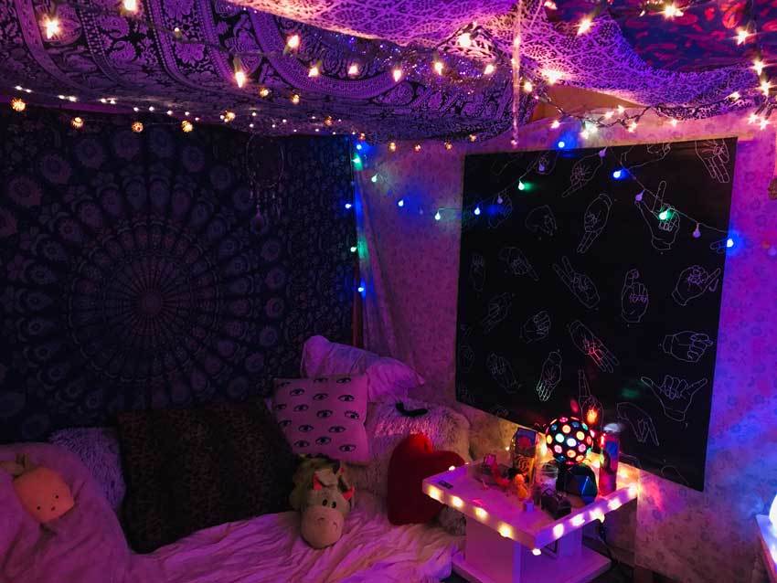 The space under a lofted bed features twinkle lights, patterned cloth, and a cozy area with a stuffed donkey.