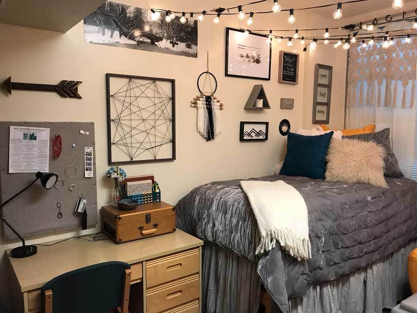 A dreamcatcher, a stylized arrow, and geometric string art decorate this wall. There is a shaggy pillow on the bed.