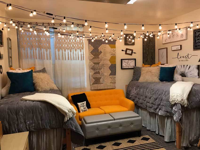 String lights cross the entire room and a bright orange couch contrasts with the gray and neutral bedding.