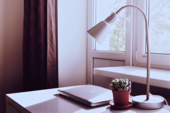 a bright desk with a lamp, a plant and a laptop