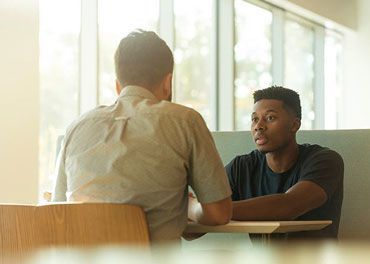 Two men sit at a table in an cafe, talking