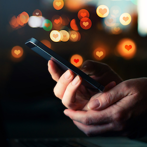 A woman's hands hold a smartphone, and little hearts float above it.