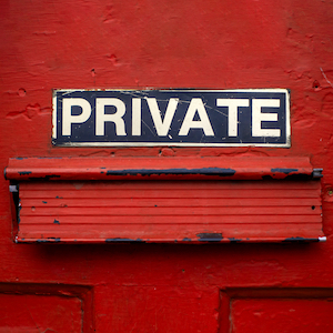 A mail delivery slot in a red door has a sign above it that says, 