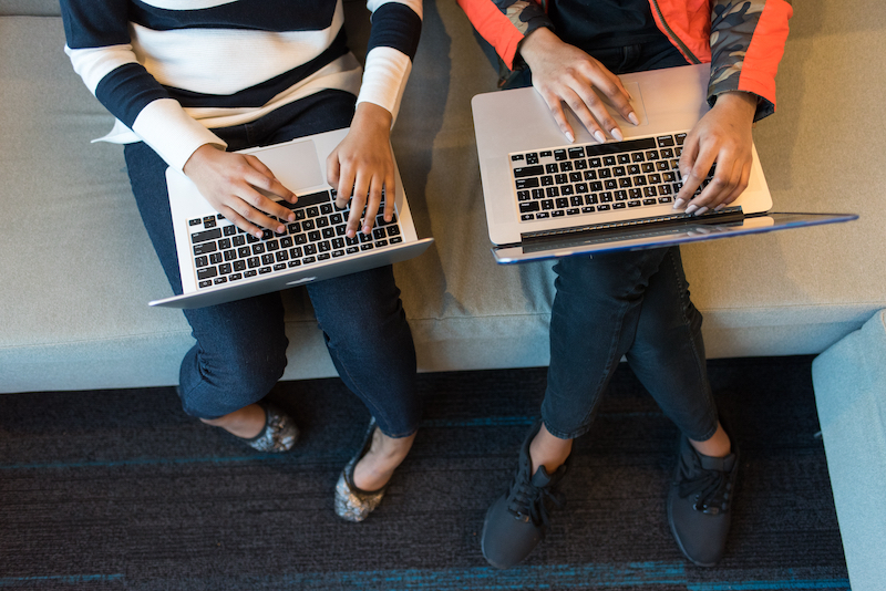 Two people sitting side by side work on laptop computers.