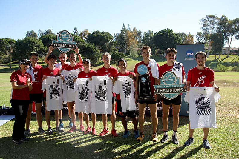 Photo of Men's Cross Country team holding two championship plaques and T-shirts