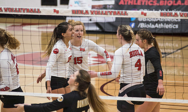 Photo of female volleyball players on the court behind the net