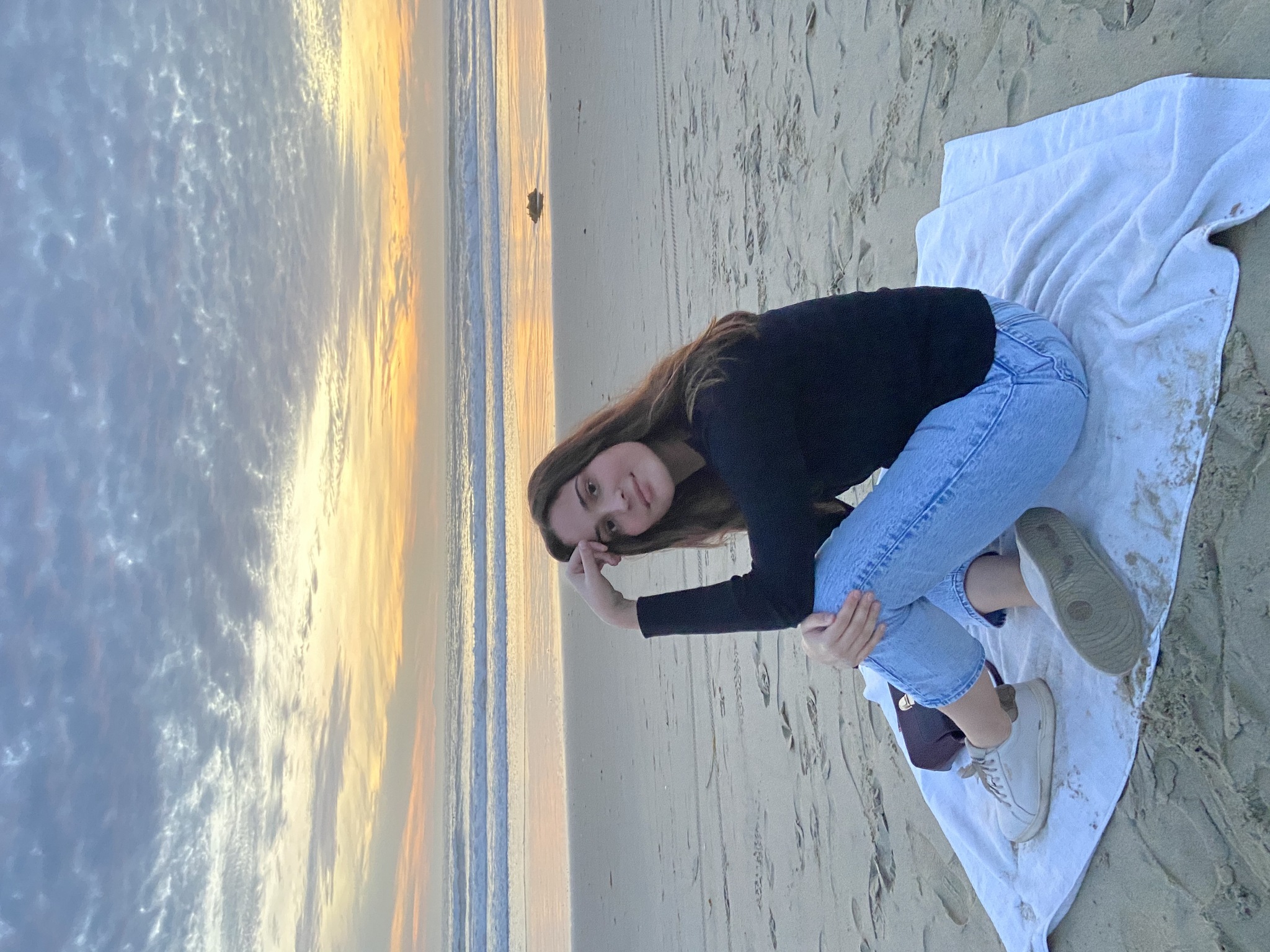 Maggie sitting on a white towel at the beach during sunset